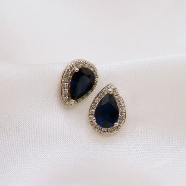 Broqueles de oro con zafiro en corte de gota, rodeados de finos destellos de diamantes que realzan su brillo y elegancia. Diseño exclusivo de Mena Fine Jewelry.