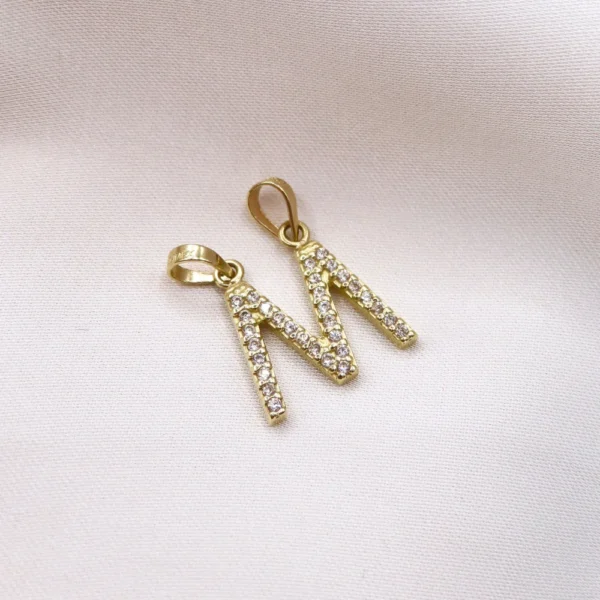 Elegante dije en forma de letra “M” elaborado en oro y engastado con brillantes circonias. Diseño exclusivo de mena Fine Jewelry.