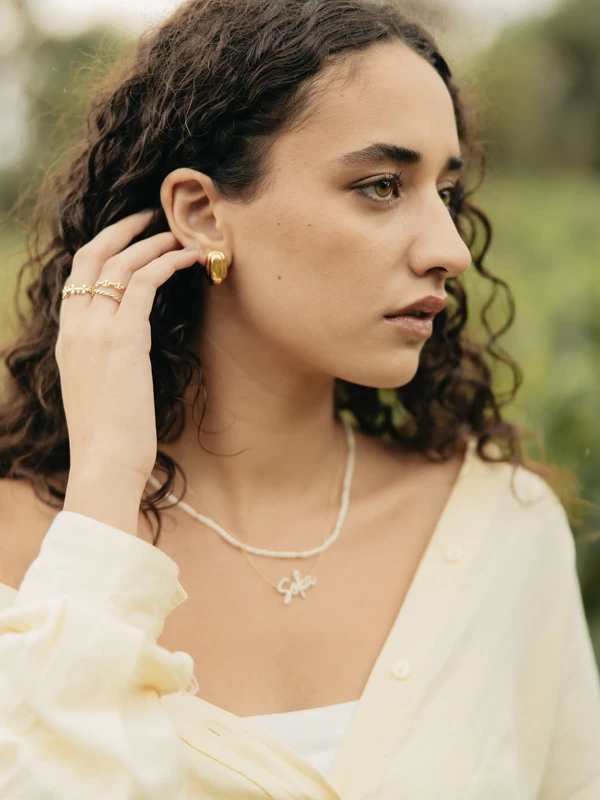 Modelo femenina luciendo aretes, anillos, una gargantilla con perlas y una cadena con dije personalizado que "Sofía". Joyería fina de Mena.