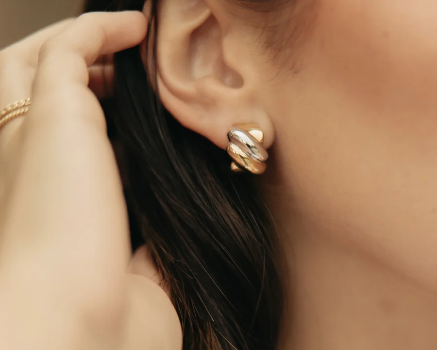 Primer plano de una modelo llevando unos aretes dorados de Mena Fine Jewelry.